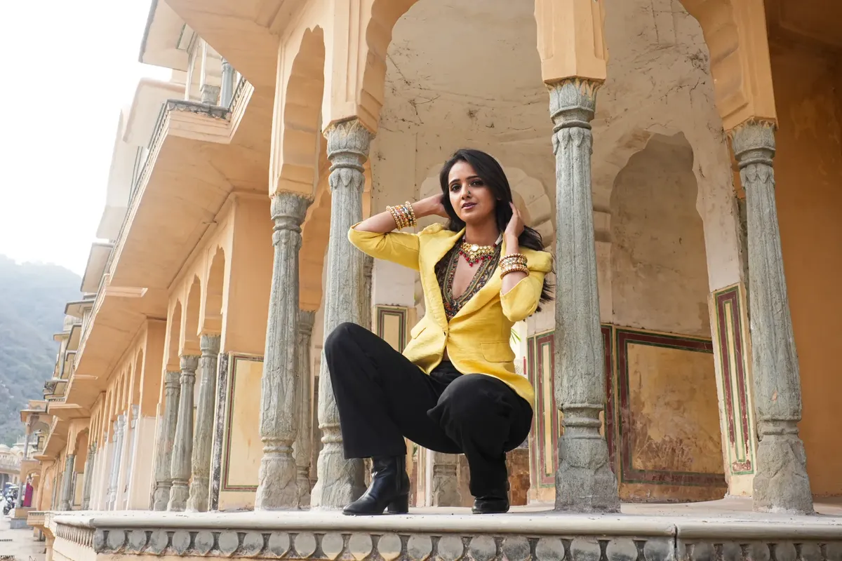 A stylish woman poses confidently in traditional Indian architectural surroundings.