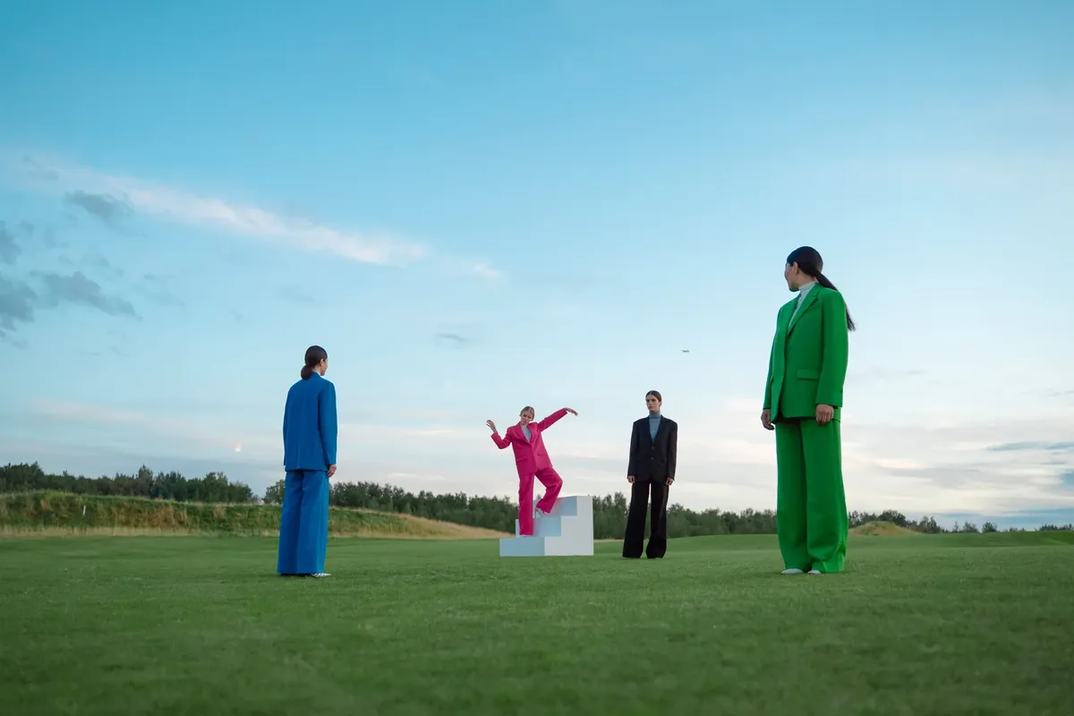 A group in vibrant suits poses creatively on a vast green field, showcasing contemporary fashion.